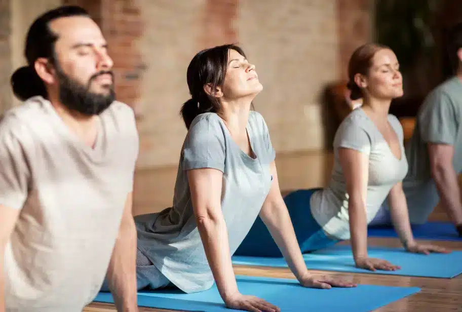 Group of people in downward-facing dog position on blue yoga mats in studio with exposed brick wall