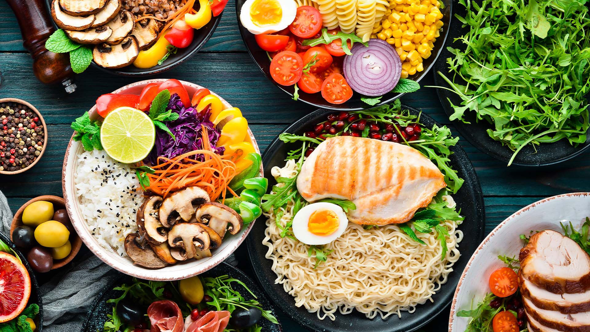 Wood table with colorful food in bowls, ramen noodles, mushrooms, onion, tomoatoes