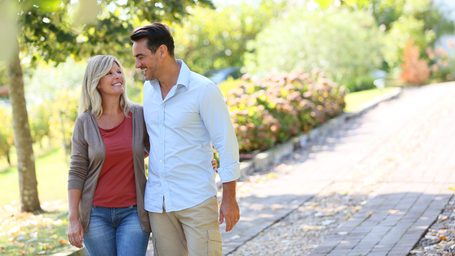 Couple on a walk in sun on brick pathway surrounded by plants and trees