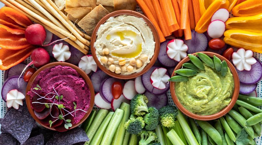 Colorful grazing snacks, hummus, guacamole, carrots, bell peppers, peas and celery