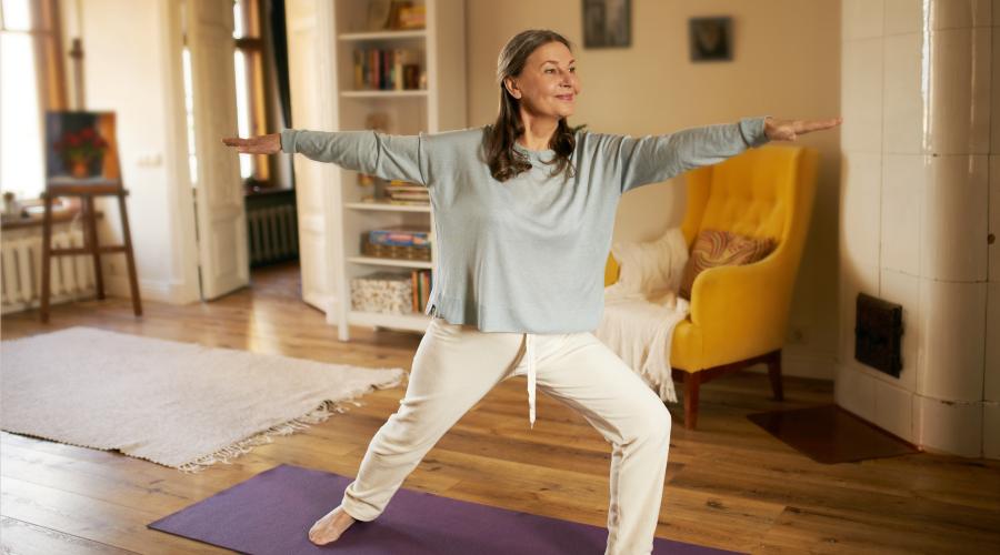 Middle aged woman in living room standing and stretching on Yoga Mat 
