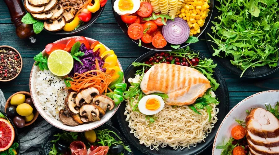 Wood table with colorful food in bowls, ramen noodles, mushrooms, onion, tomoatoes