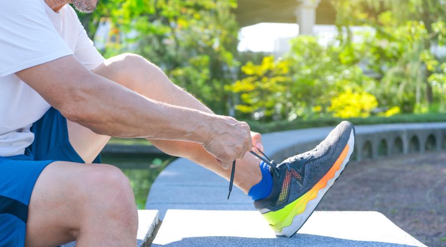 Man sitting outside in sun, lacing up vibrant colored running shoes