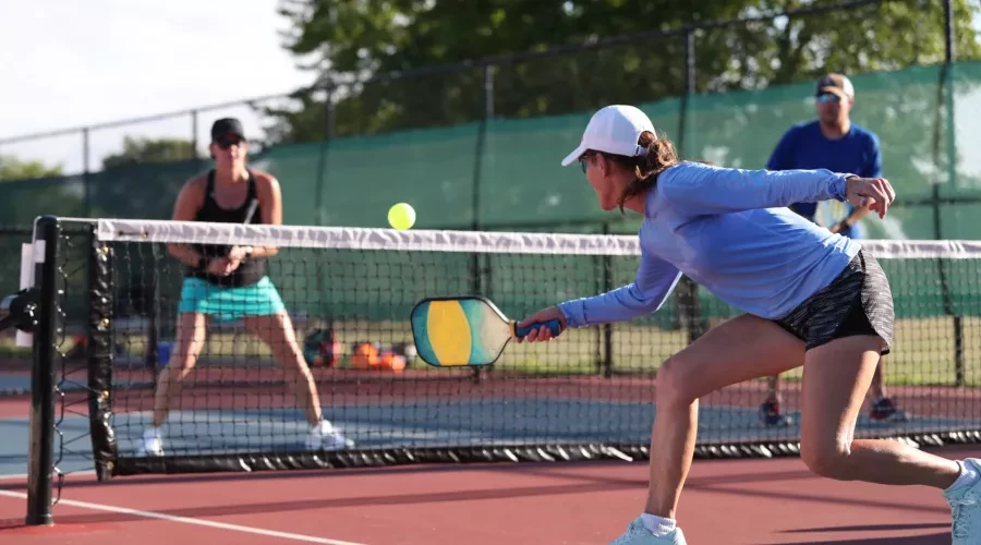 Two women in athletic gear, playing PickleBall on Tennis Court