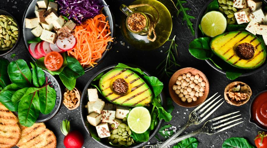 Table full of bowls with colorful foods in them, Avocado, tofu, spinach, carrots, Seeds and beans