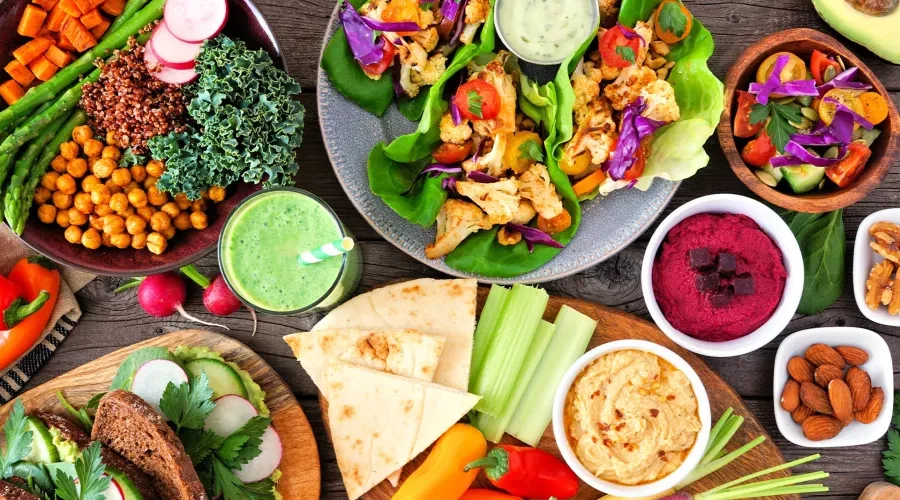 Wood table with bowls of colorful food, lettuce wraps, pita bread, hummus, vegetables and nuts
