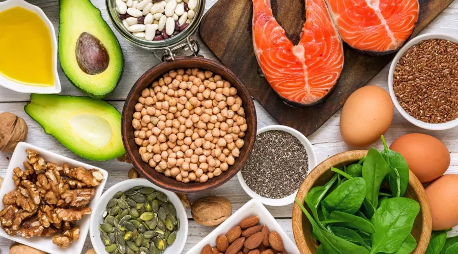 wood table with bowl of garbanzo beans, cut avocado, fresh salmon, bowl of spinach and various nuts