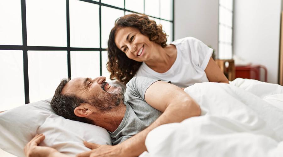 middle aged couple in bed, smiling at each other 
