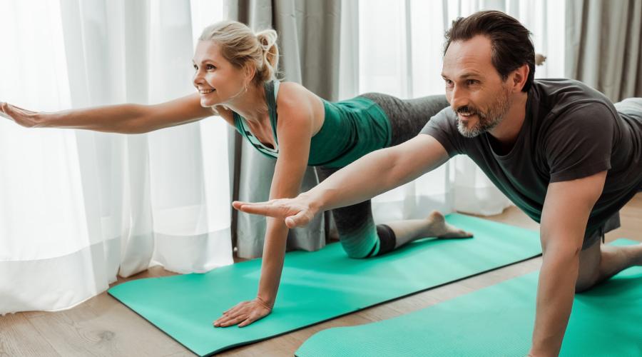 Middle-aged couple stretching out arms and legs on yoga mat indoors