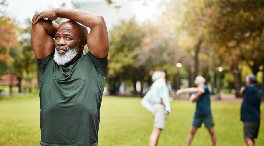 African American man with gray beard, in park with other men stretching