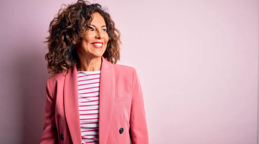woman with brown curly hair and pink blazer, smiling