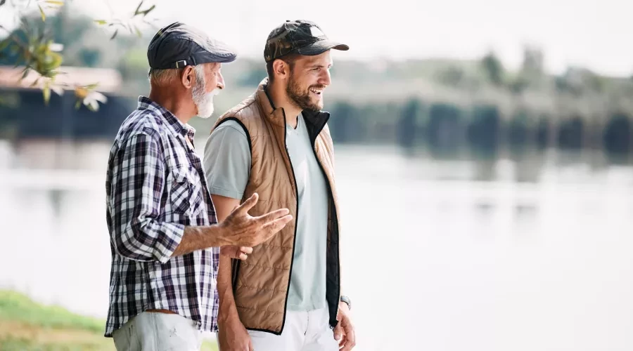 Middle-aged man walking and talking with senior gentleman outside by lake