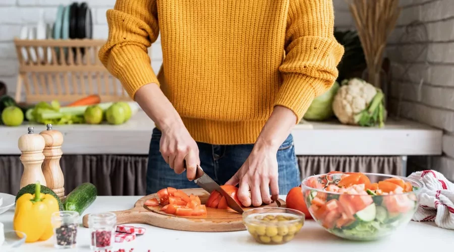 Woman in kitchen cutting tomatoes on cutting board, surrounded by vegetables