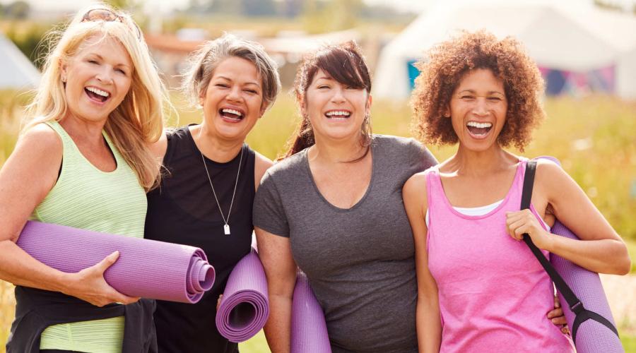 4 middle aged women, with workout clothes and yoga mats, smiling