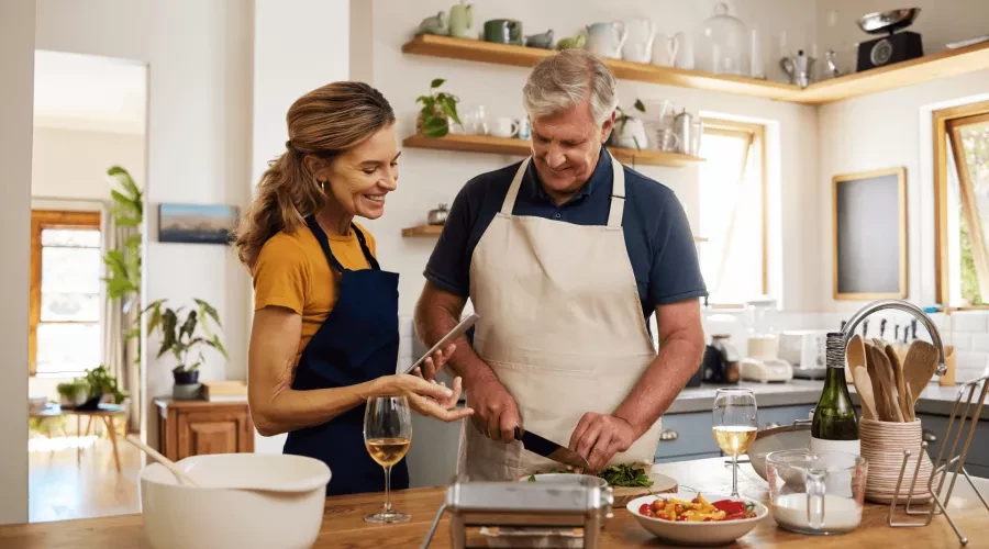 Woman smiling and looking at phone recipe, watching man prepare food on cutting board in kitchen with wine glasses