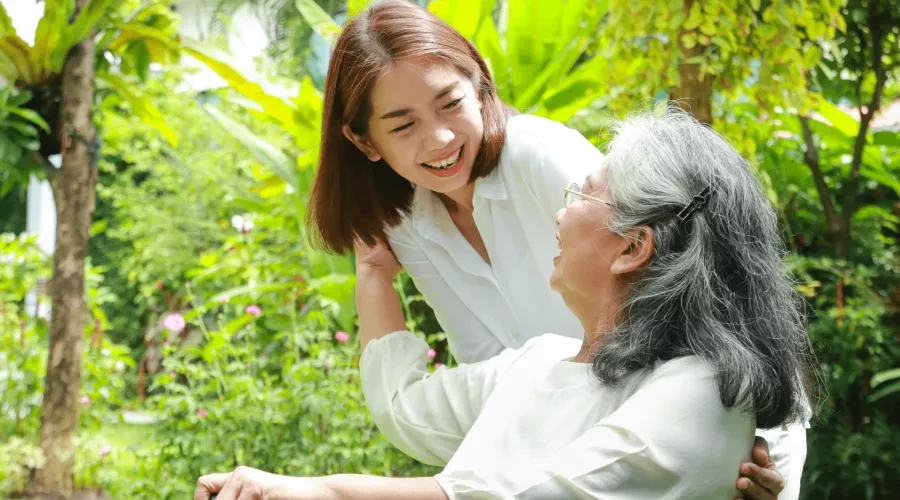 younger caregiver smiling at senior sitting in chair with cane and smiling back