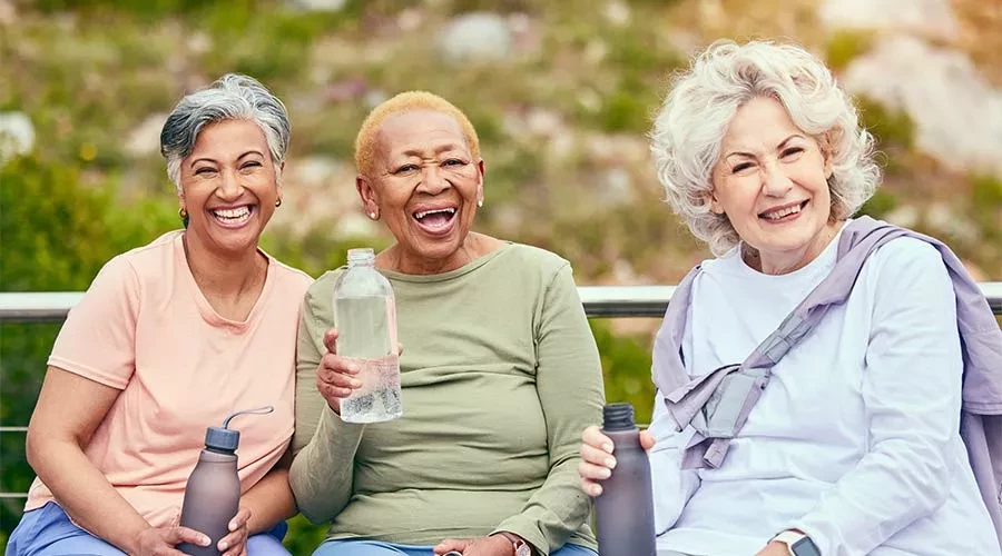 3 senior women outside sitting on bench smiling