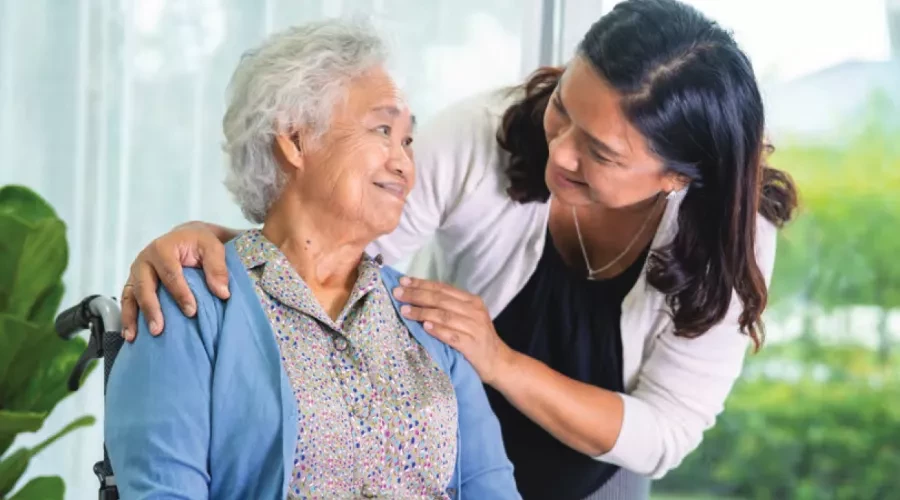 Caregiver leaning over and smiling at elderly woman in wheelchair