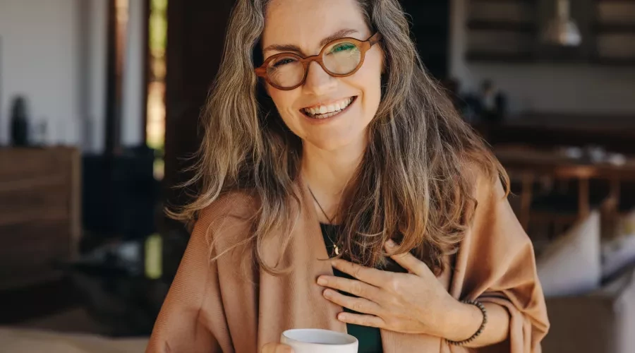 middle aged woman, hand over heart, smiling and holding coffee mug
