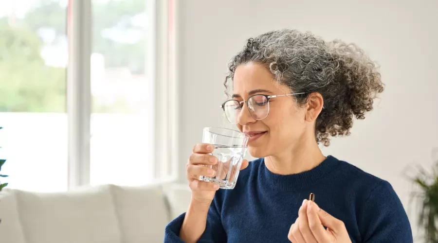 woman in blue shirt, taking pill with water