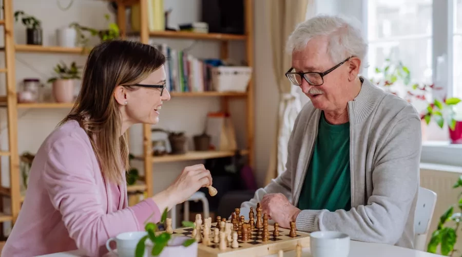Caregiver smiling and playing chess with elderly man
