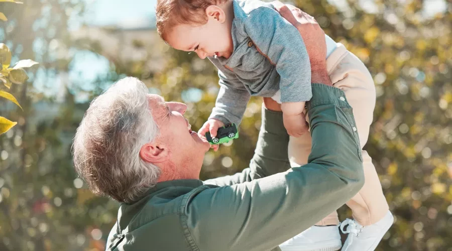 older man holding up his grandson and smiling
