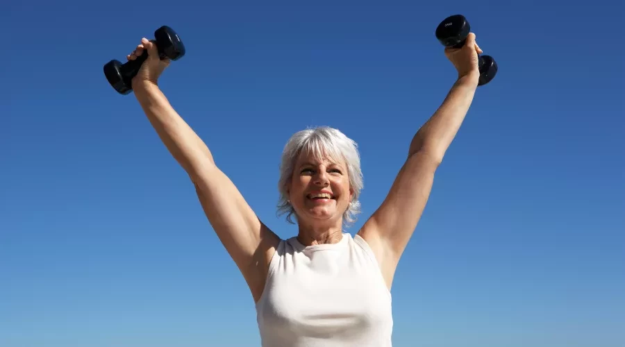Woman outside holding weights above her head and smiling