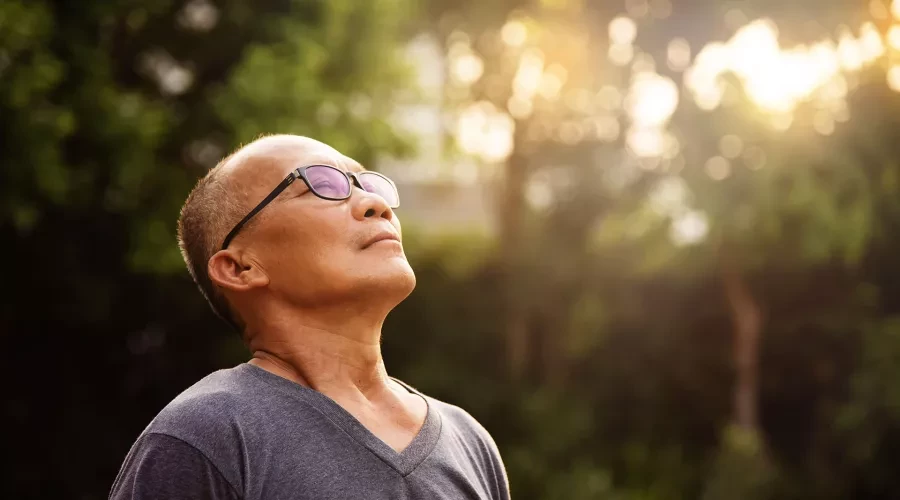 Man taking a deep breath of fresh air with his eyes closed and head tilted back, basking in the golden morning light.
