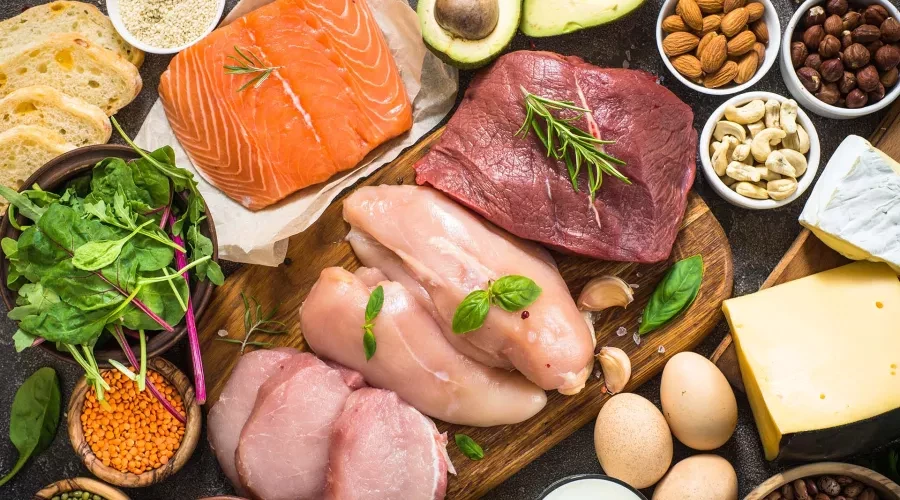 Table with Salmon, fresh chicken, pork and beef cuts surrounded by bowls of nuts, vegetables and eggs
