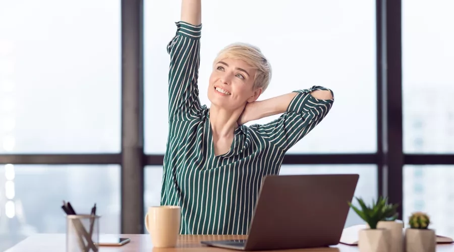 Woman in an office stretches her arms and neck while seated in her desk chair.