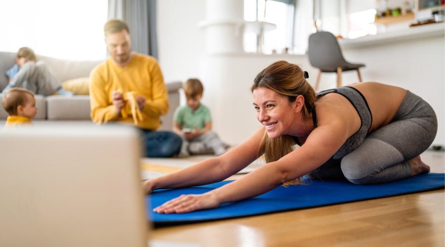 Woman doing Yoga on mat in living room surrounded by husband and 2 kids