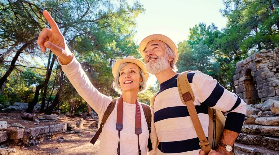 An older couple wearing hats and backpacks, the woman with a camera around her neck, enjoying nature while out on a hike.