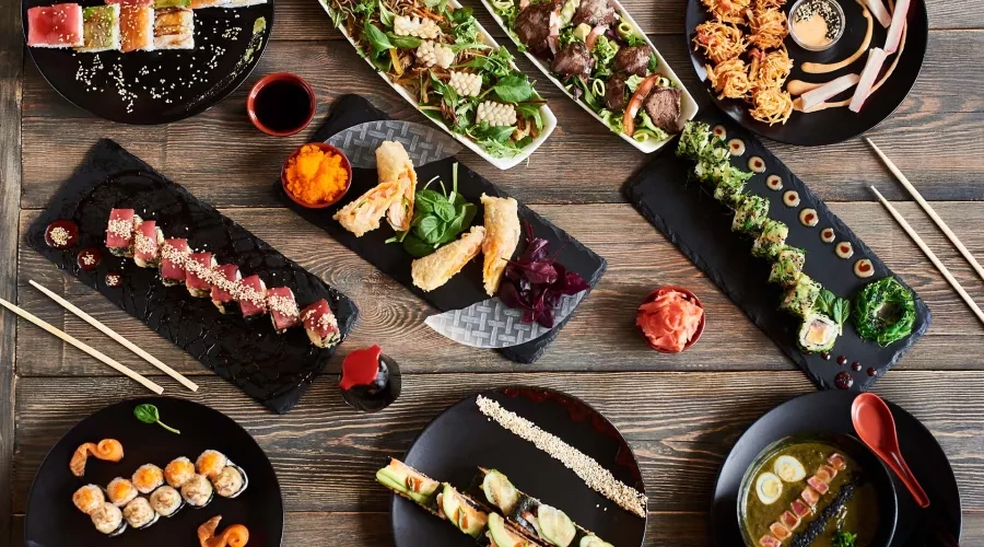 A table laid out with Japanese food including sushi, tempura, soup and fresh vegetable garnishes.