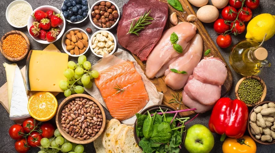 Table full of colorful food, including raw Salmon, chicken breasts, grains and vibrant fruits
