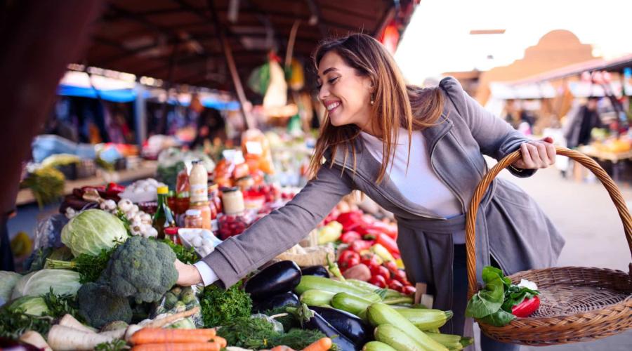 Woman with basket at farmers market choosing fresh vegetables
