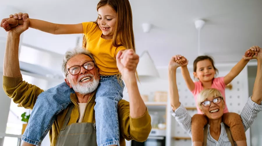 Grandparents smiling holding 2 small smiling girls on their shoulders and locking hands