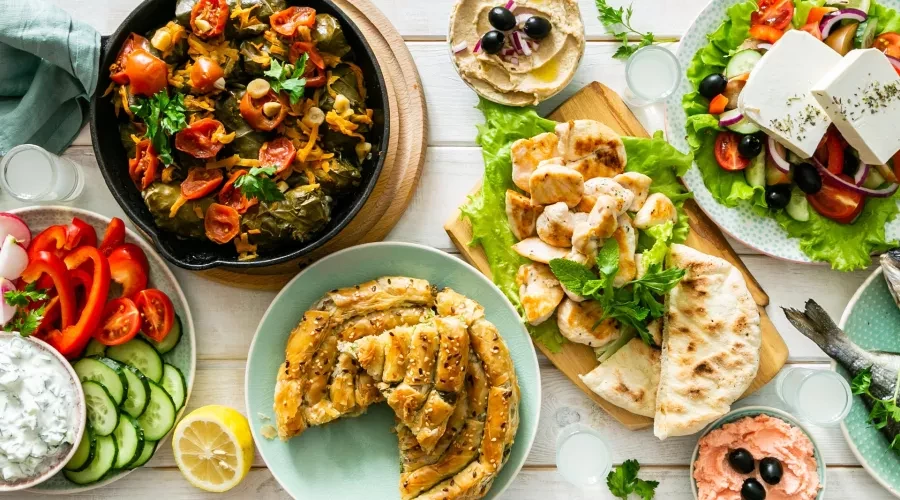 White Wood table with vibrant Greek Food, Salad, Pastry, Chicken and Yogurt Dip