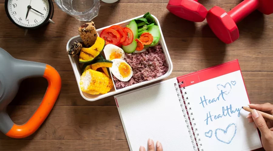Wood table with power meal, weights, clock and notepad with words Heart Healthy written on it
