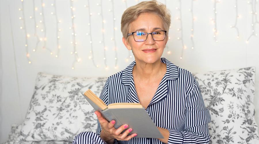 Older woman in pajamas on couch reading a book in the evening