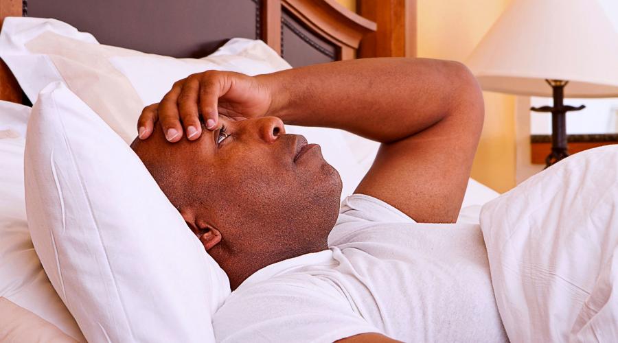 Man laying in bed stressed with hand on his forehead