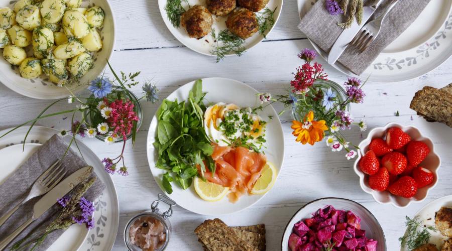 White wood table with colorful plates of food, including salmon lox, eggs, potatoes, meatballs and strawberries