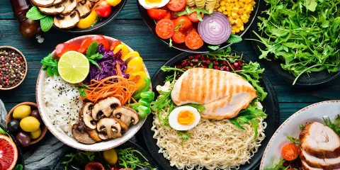 Wood table with colorful food in bowls, ramen noodles, mushrooms, onion, tomoatoes