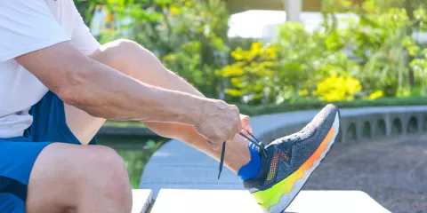 Man sitting outside in sun, lacing up vibrant colored running shoes