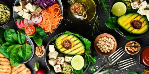 Table full of bowls with colorful foods in them, Avocado, tofu, spinach, carrots, Seeds and beans