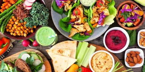 Wood table with bowls of colorful food, lettuce wraps, pita bread, hummus, vegetables and nuts