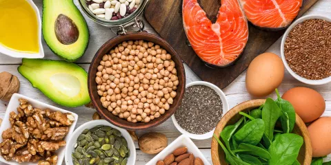 wood table with bowl of garbanzo beans, cut avocado, fresh salmon, bowl of spinach and various nuts
