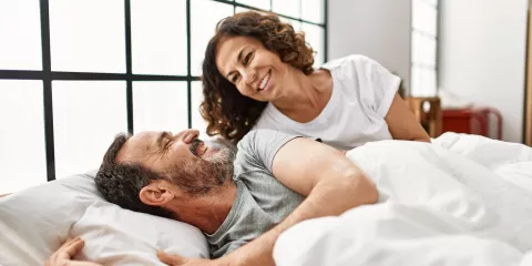 middle aged couple in bed, smiling at each other 