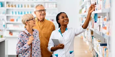 Pharmacist smiling and showing senior couple supplements on shelf in Pharmacy