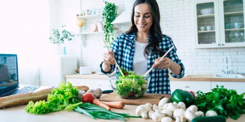 Woman in kitchen mixing a salad surrounded by various vegetables