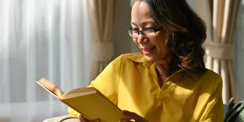 Woman in glasses reading book in living room chair and smiling